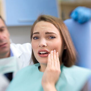 Woman in dental chair holding cheek