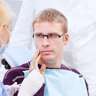 Young man in dental chair holding cheek