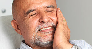 Man in dental chair holding cheek in pain